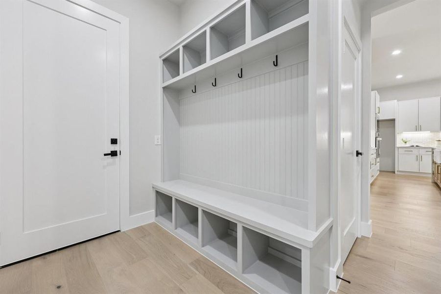 Entryway with light hardwood floors, featuring a white built-in storage unit with cubbies and hooks, and a white door with black hardware
