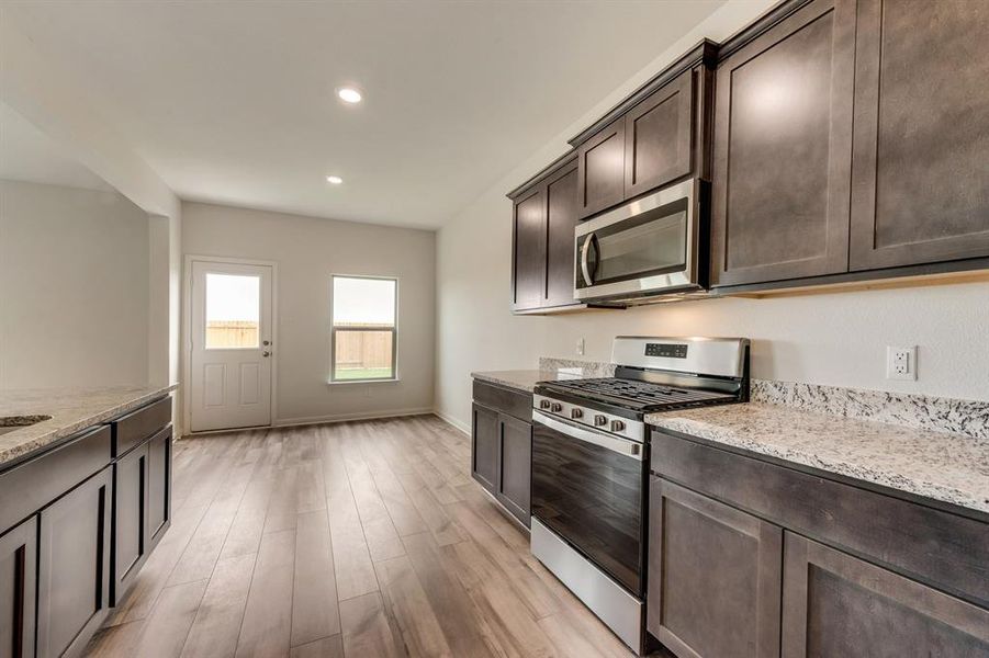 Kitchen featuring appliances with stainless steel finishes, dark brown cabinetry, light wood-type flooring, and light stone counters