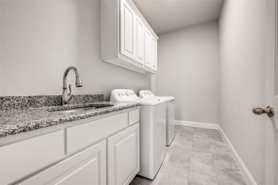 Clothes washing area featuring light tile patterned flooring, washing machine and clothes dryer, cabinets, and sink