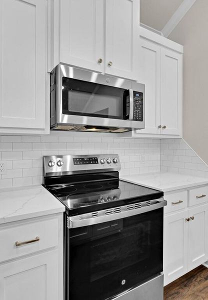 Kitchen with stainless steel appliances, tasteful backsplash, white cabinets, light stone counters, and ornamental molding