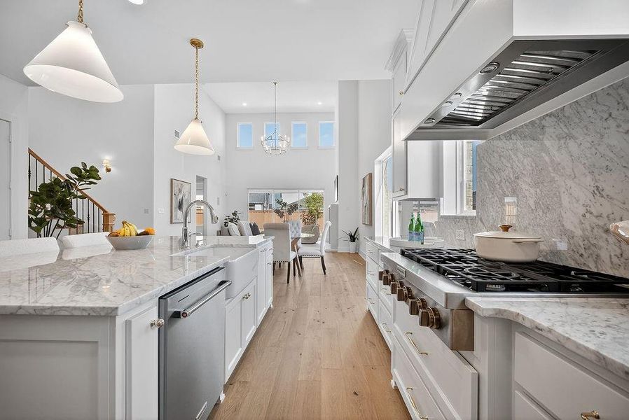 Kitchen featuring light stone countertops, white cabinets, wall chimney exhaust hood, appliances with stainless steel finishes, and a towering ceiling Kitchen featuring light stone countertops, white cabinets, wall chimney exhaust hood, appliances with stainless steel finishes, and a towering ceiling