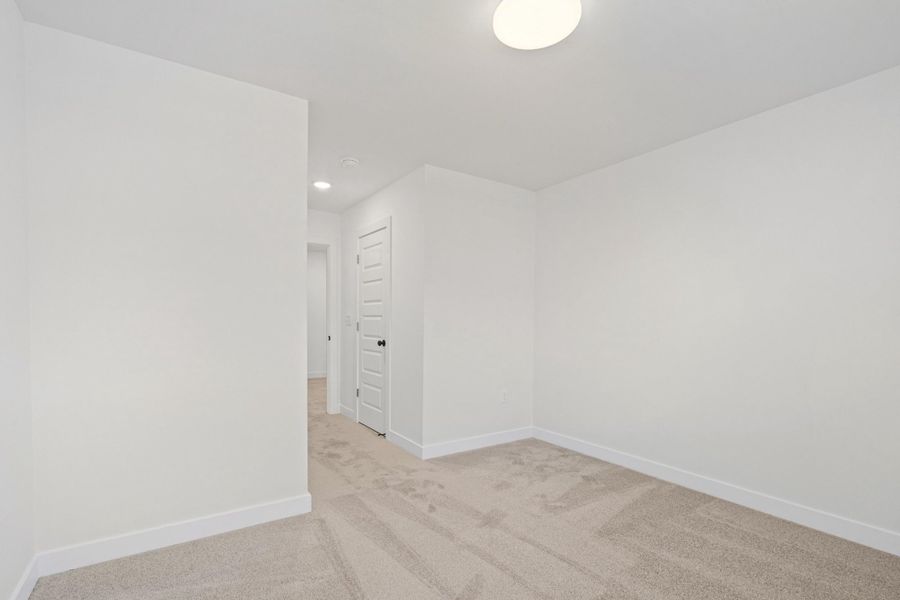 Neutral-toned carpeted room featuring bright white walls, crisp baseboards, and a contemporary flush-mount ceiling light fixture