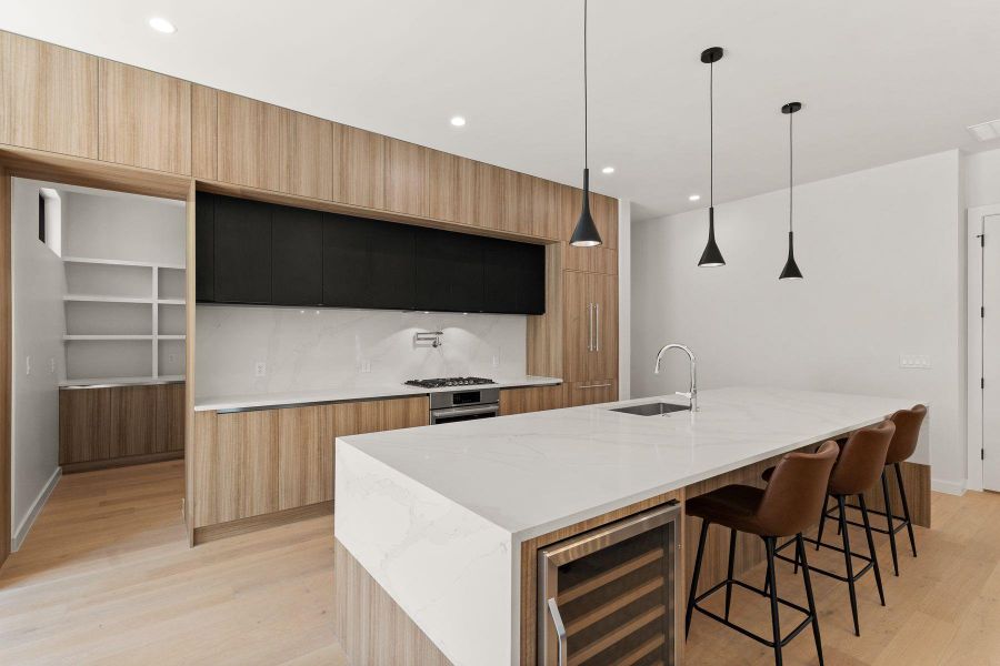 Minimalist cabinetry pairs with light wood flooring and stone countertops in this modern culinary space.