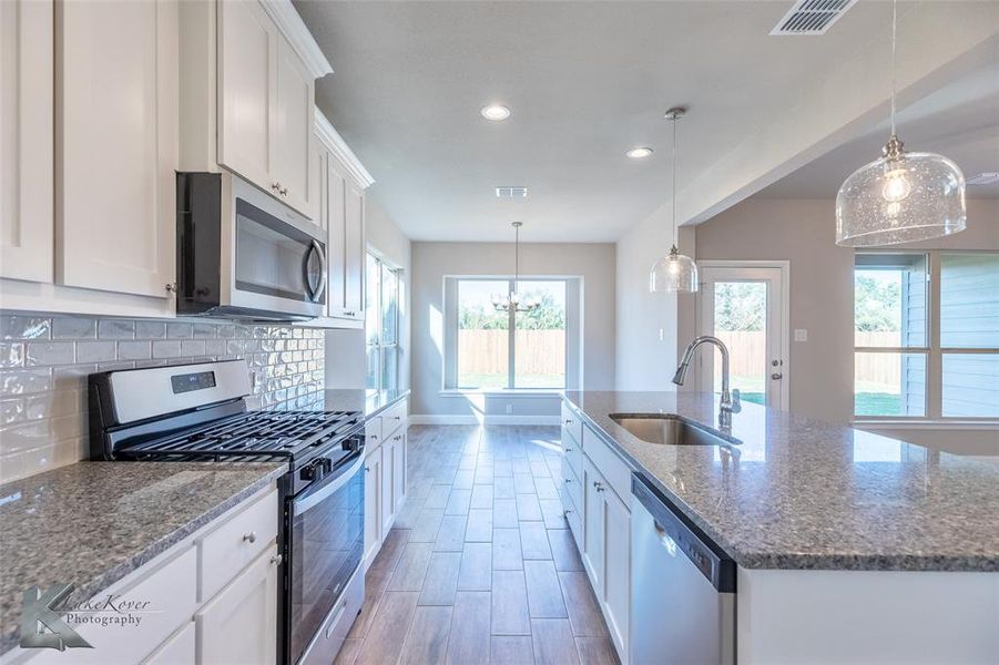 Kitchen featuring stainless steel appliances, hanging light fixtures, white cabinetry, dark stone countertops, and recessed lighting