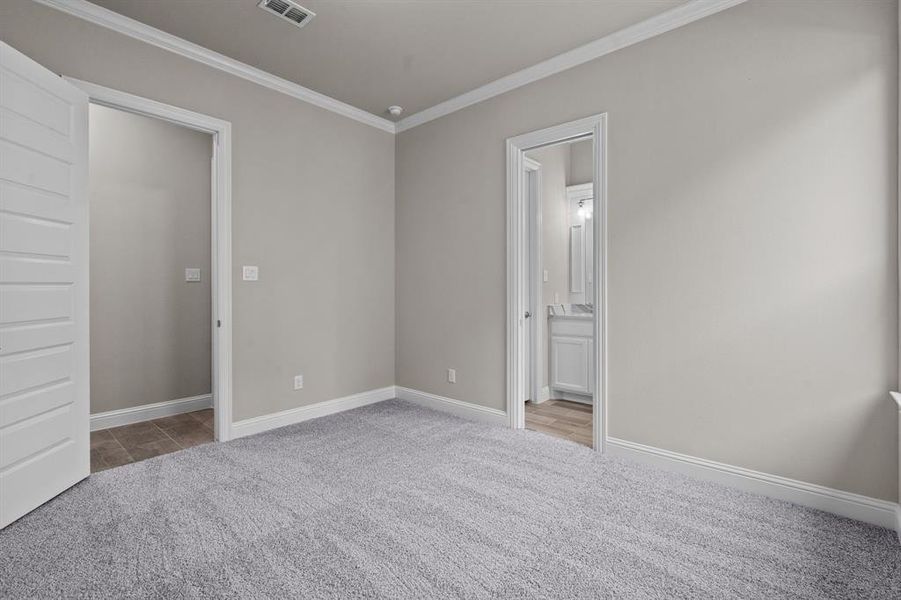 Unfurnished bedroom featuring crown molding, ensuite bath, and light colored carpet. Not actual home. Previous built example.