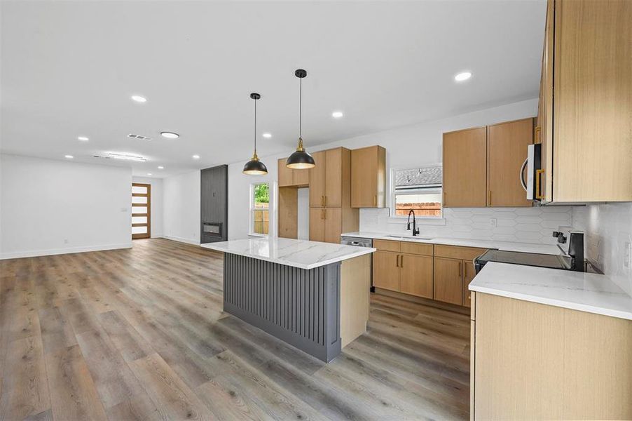 Kitchen featuring light hardwood / wood-style floors, a kitchen island, appliances with stainless steel finishes, sink, and tasteful backsplash