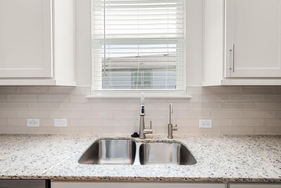 A well-lit kitchen features a double basin stainless steel sink and speckled granite countertops, complemented by a subway tile backsplash. A well-lit kitchen features a double basin stainless steel sink and speckled granite countertops, complemented by a subway tile backsplash.