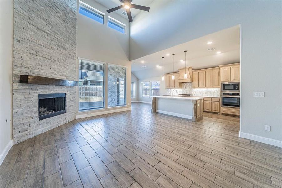 Spacious living area featuring a floor-to-ceiling stacked stone fireplace with a wood mantle, wood-finish tile flooring, and a vaulted ceiling with a ceiling fan