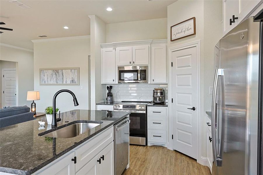 Kitchen featuring a dark stone countertop island with an undermount sink, white cabinetry, stainless steel appliances, a subway tile backsplash, and light wood-finish flooring