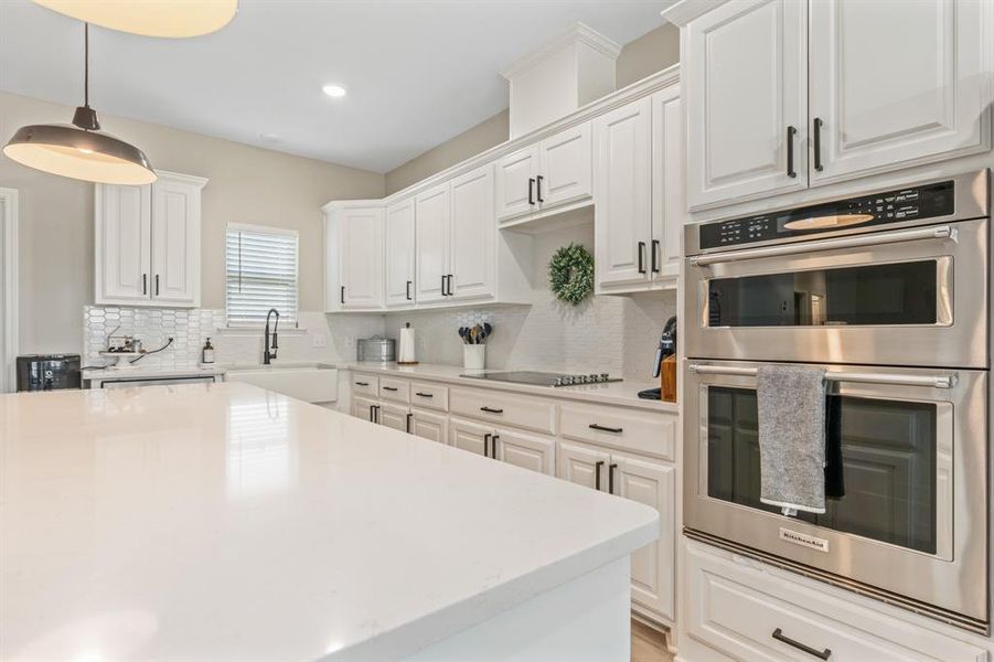 Kitchen with built ins, tasteful backsplash, white cabinetry, light stone countertops, and decorative light fixtures Kitchen with built ins, tasteful backsplash, white cabinetry, light stone countertops, and decorative light fixtures