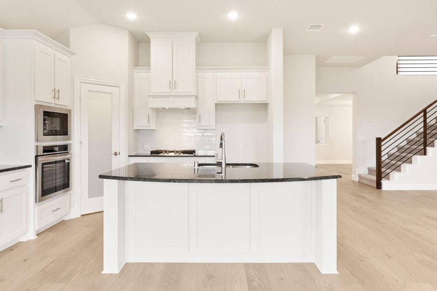 Kitchen with white cabinets, dark granite island, stainless steel appliances, and light hardwood floors