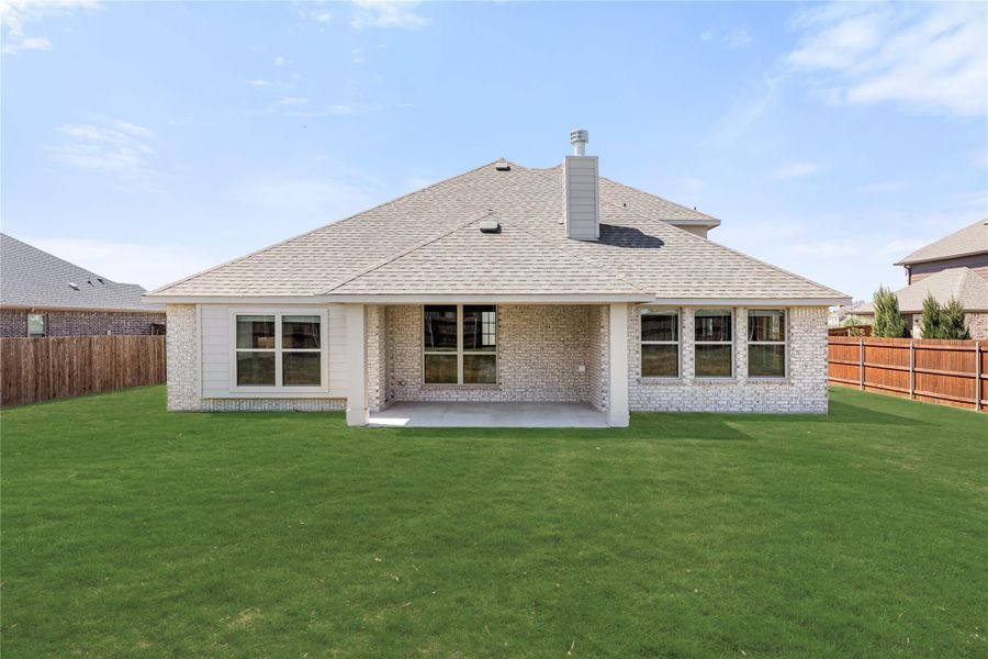 Rear view of single-story brick home with covered patio, large backyard, and wood privacy fence.