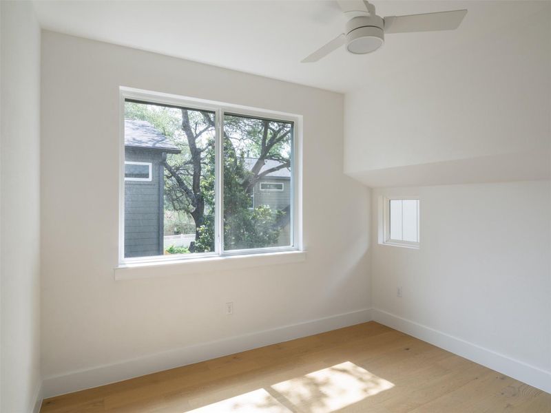 Bright interior space featuring a contemporary ceiling fan, wood-finish flooring, and multiple windows allowing for natural light