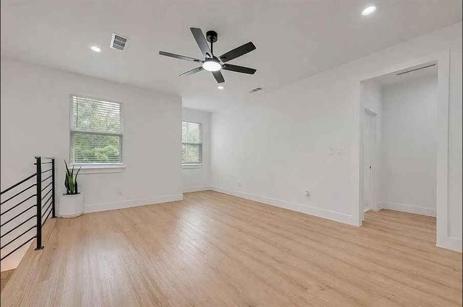 Spacious interior room featuring light wood-finish flooring, recessed lighting, and a contemporary ceiling fan