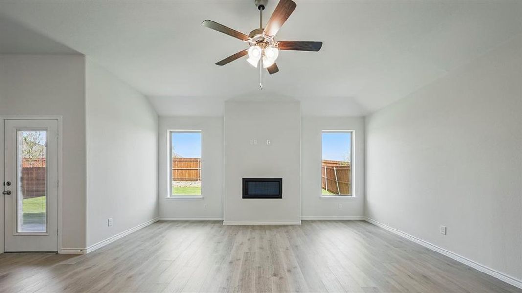 Unfurnished living room featuring light wood-style floors, plenty of natural light, a glass covered fireplace, and ceiling fan