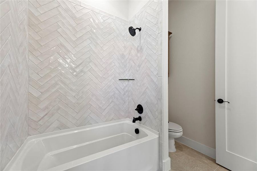 Bathroom featuring tiled shower / bath, tile patterned floors, and toilet