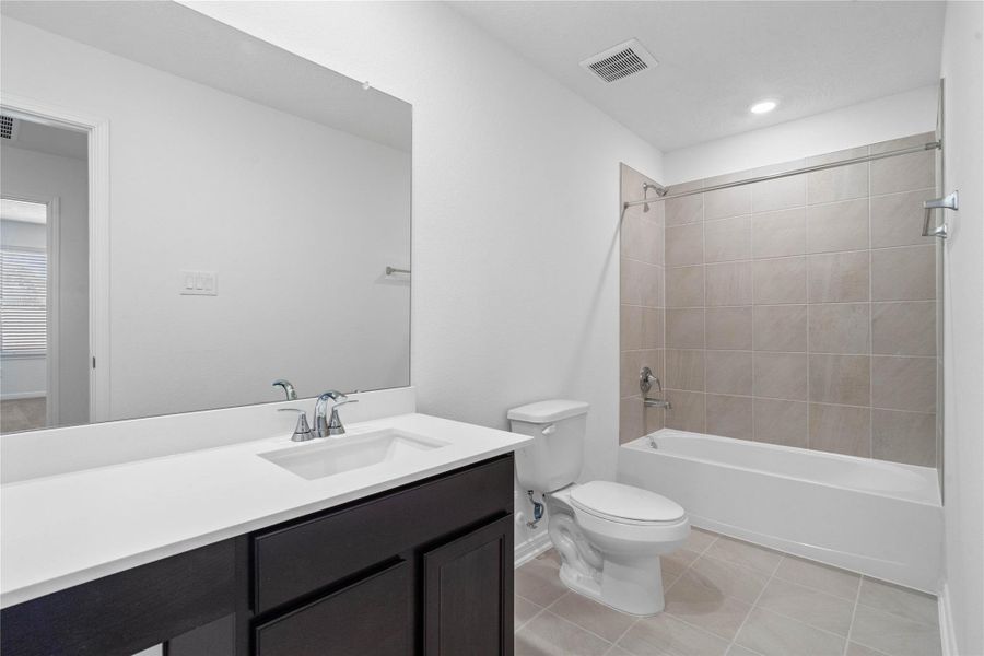 The secondary bathroom showcases tile flooring, a bath/shower combo with Daltile tile surround, a vanity with knee space and stunning light countertop, a mirror, sleek fixtures, and contemporary finishes throughout.