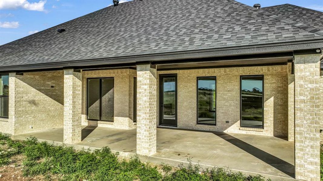 Back of house featuring a shingled roof, brick siding, and a patio Back of house featuring a shingled roof, brick siding, and a patio