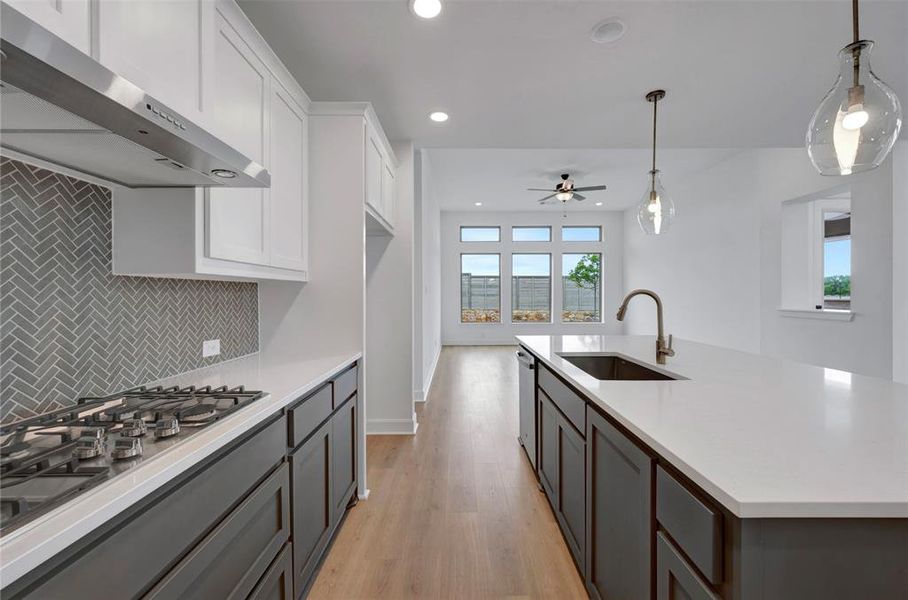 Well-appointed kitchen featuring a gas range with an overhead exhaust hood, a subway tile backsplash, and an island with a sink and pendant lighting