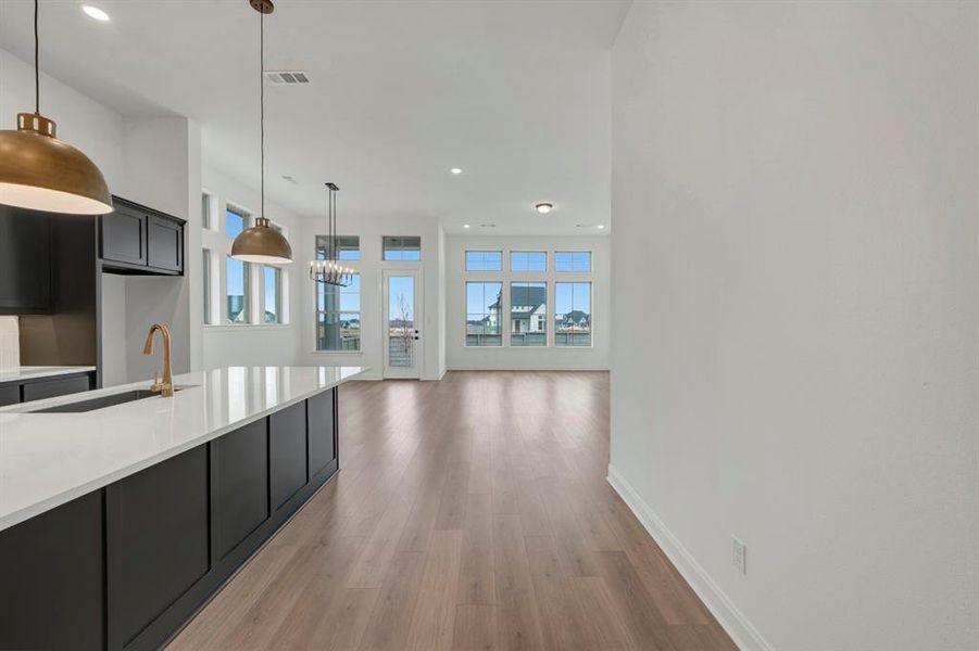Kitchen featuring light stone counters, light wood-style flooring, dark cabinets, and hanging light fixtures