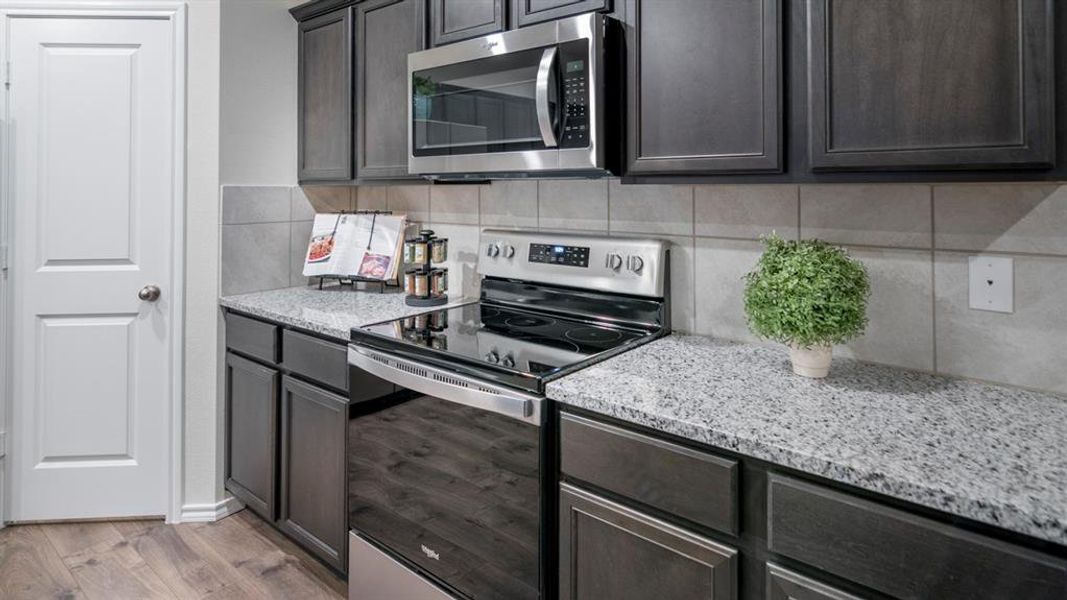 Kitchen featuring stainless steel appliances, light stone counters, light wood-style flooring, and dark wood finish cabinetry