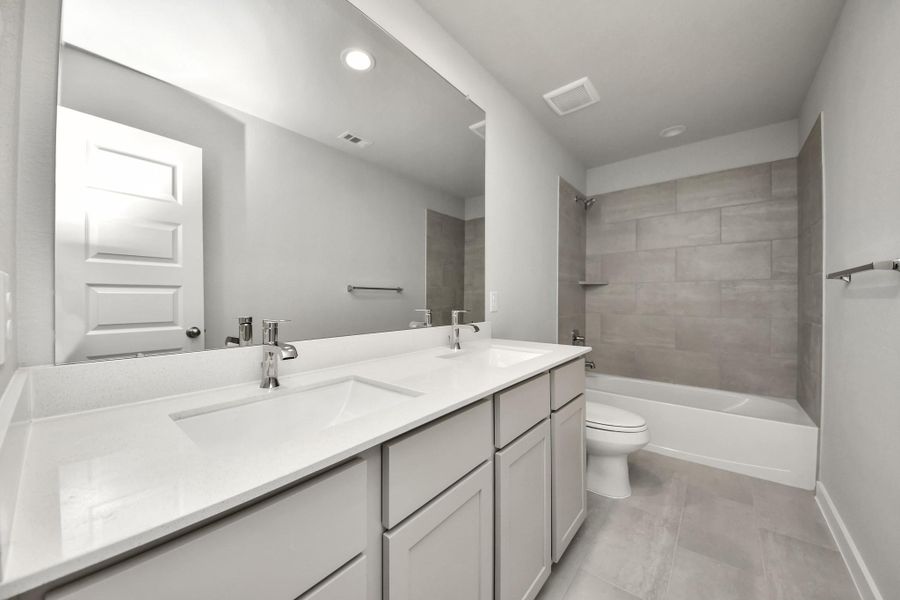 Secondary bath features tile flooring, bath/shower combo with tile surround, light stained wood cabinets, beautiful light countertop. Sample photo of completed home with similar floor plan. Actual colors and selections may vary.