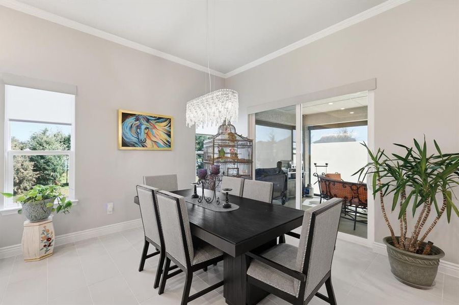Dining area featuring tile flooring, crown molding, a rectangular chandelier, a window with exterior views, and sliding glass doors opening to an outdoor patio