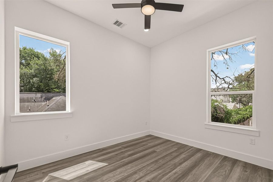 This bright room features large windows with scenic views, modern light wood flooring, and a ceiling fan, offering a fresh and airy atmosphere. This bright room features large windows with scenic views, modern light wood flooring, and a ceiling fan, offering a fresh and airy atmosphere.