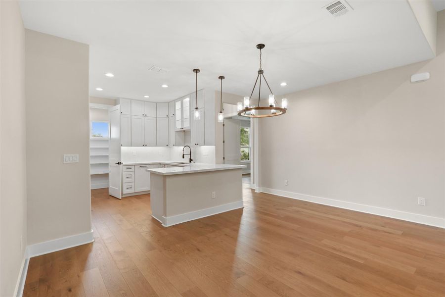 Kitchen featuring a sink, visible vents, light countertops, light wood-type flooring, and a notable chandelier Kitchen featuring a sink, visible vents, light countertops, light wood-type flooring, and a notable chandelier