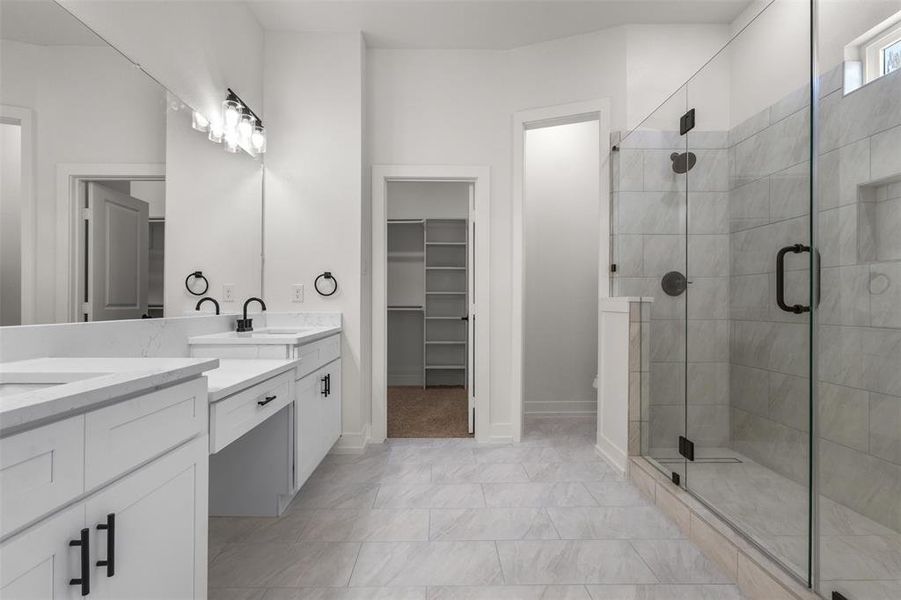 Well-appointed bathroom featuring a double vanity with stone countertops, a spacious glass-enclosed shower, and sleek black fixtures