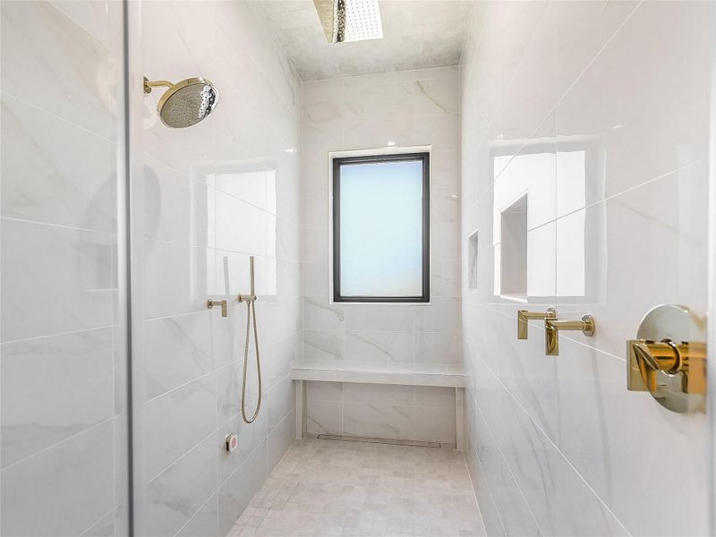 The spacious shower features polished gold fixtures, an overhead rain shower, and a built-in bench