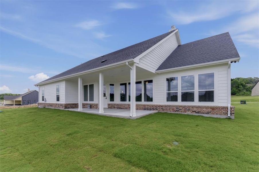Rear exterior featuring a covered patio, extensive lawn, white siding, dark shingle roof, and brick foundation
