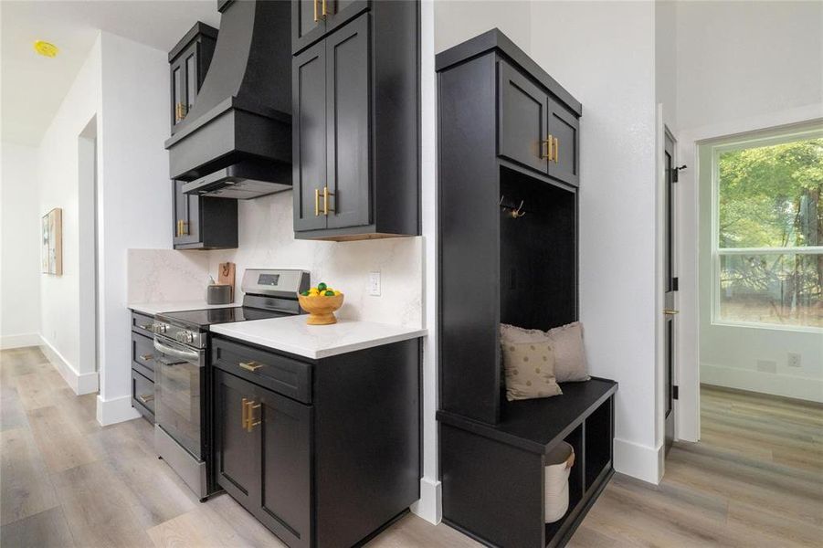 Kitchen featuring backsplash, stainless steel stove, light wood-type flooring, and custom exhaust hood