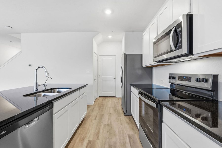 Kitchen featuring wood-finish flooring, white cabinetry, dark countertops, and stainless steel appliances including a refrigerator, range, microwave, and dishwasher