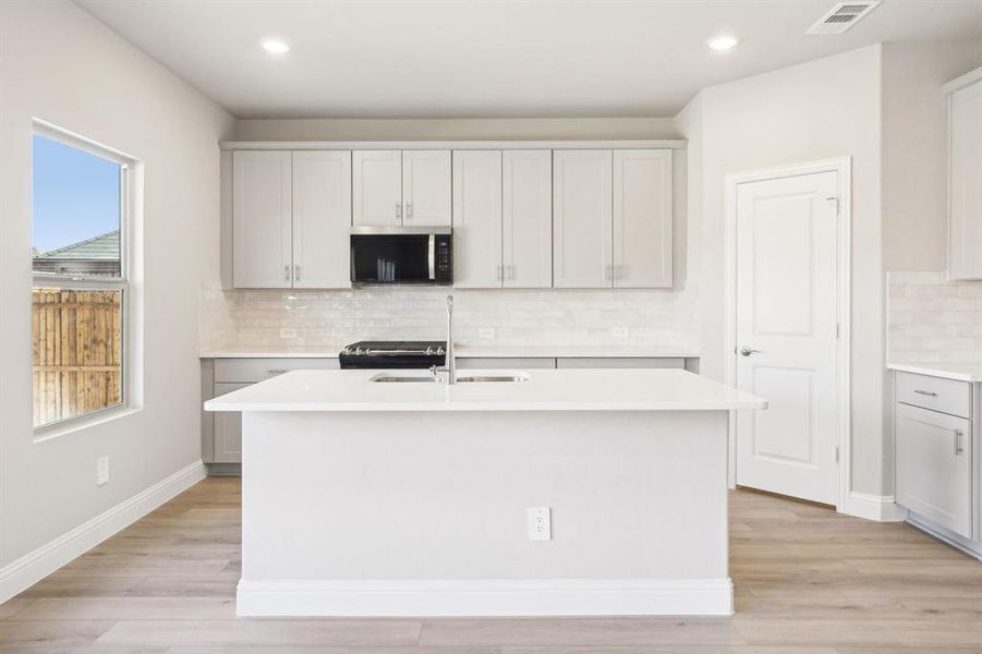 Kitchen featuring decorative backsplash, stainless steel microwave, light wood finished floors, an island with sink, and recessed lighting Kitchen featuring decorative backsplash, stainless steel microwave, light wood finished floors, an island with sink, and recessed lighting