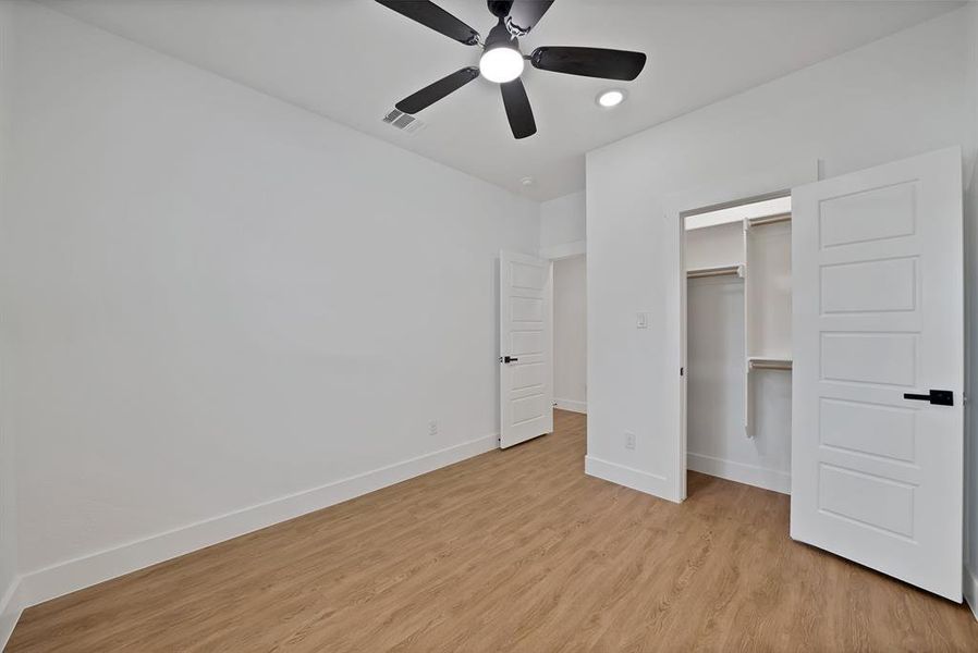 Unfurnished bedroom with light wood finished floors, ceiling fan, a spacious closet, and recessed lighting