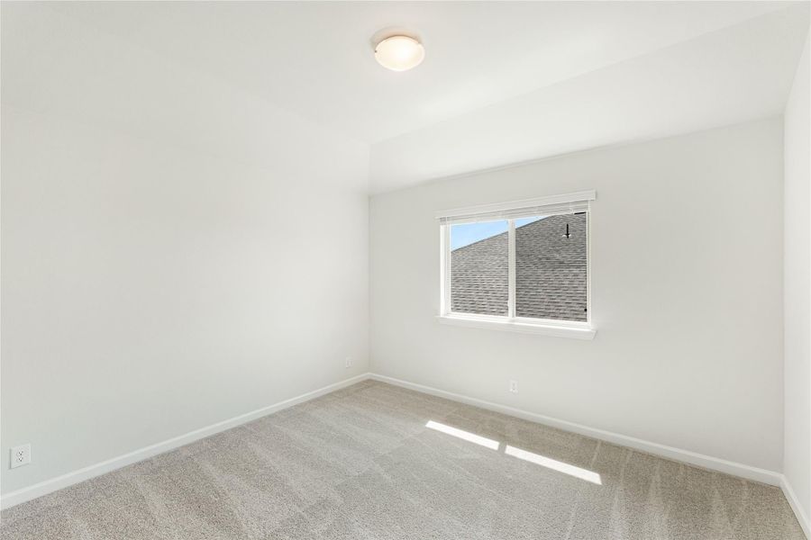 Empty bedroom with white walls, beige carpet, vaulted ceiling, and single window