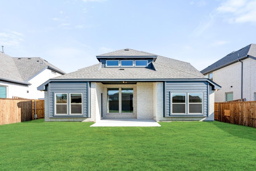 Home's rear exterior with brick and blue siding, covered patio, large windows, and fenced green backyard. Home's rear exterior with brick and blue siding, covered patio, large windows, and fenced green backyard.