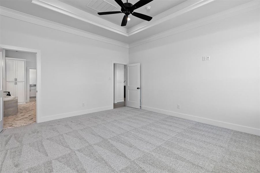 Unfurnished bedroom featuring a tray ceiling, ceiling fan, light carpet, and ensuite bathroom