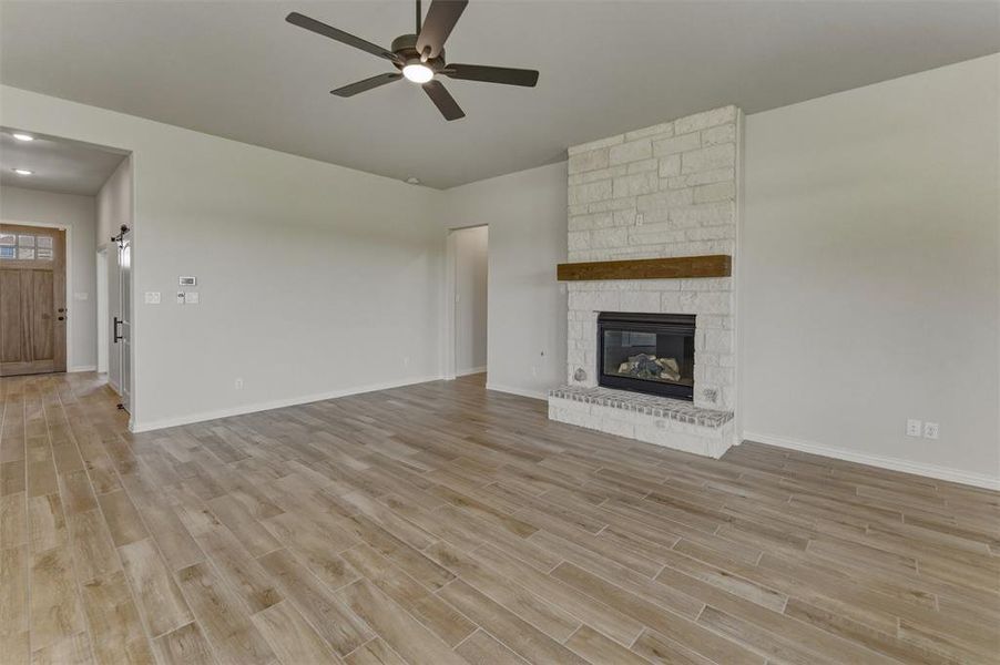 Living space featuring wood-finish flooring, a stone-clad fireplace with a timber mantel, a ceiling fan with integrated lighting, and recessed ceiling lights Living space featuring wood-finish flooring, a stone-clad fireplace with a timber mantel, a ceiling fan with integrated lighting, and recessed ceiling lights