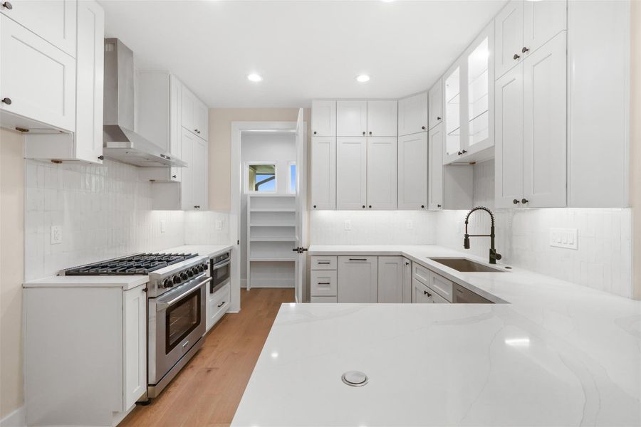 Kitchen featuring high end range, light stone counters, wall chimney range hood, and a sink Kitchen featuring high end range, light stone counters, wall chimney range hood, and a sink