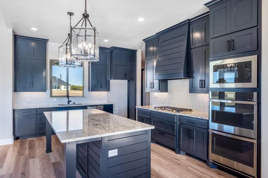 Kitchen with a kitchen island, light wood-type flooring, premium range hood, and appliances with stainless steel finishes