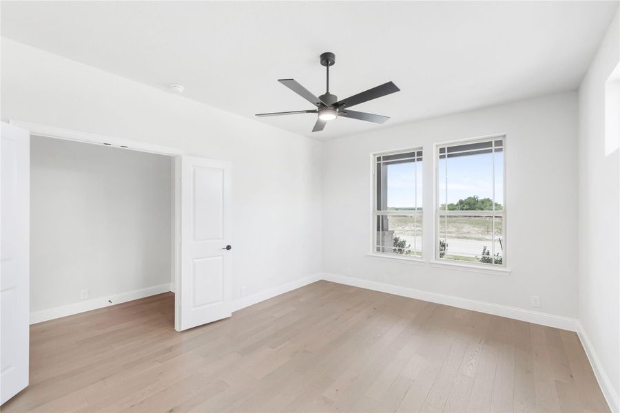 Empty bedroom with light wood floors, black ceiling fan, and large window with outdoor view Empty bedroom with light wood floors, black ceiling fan, and large window with outdoor view