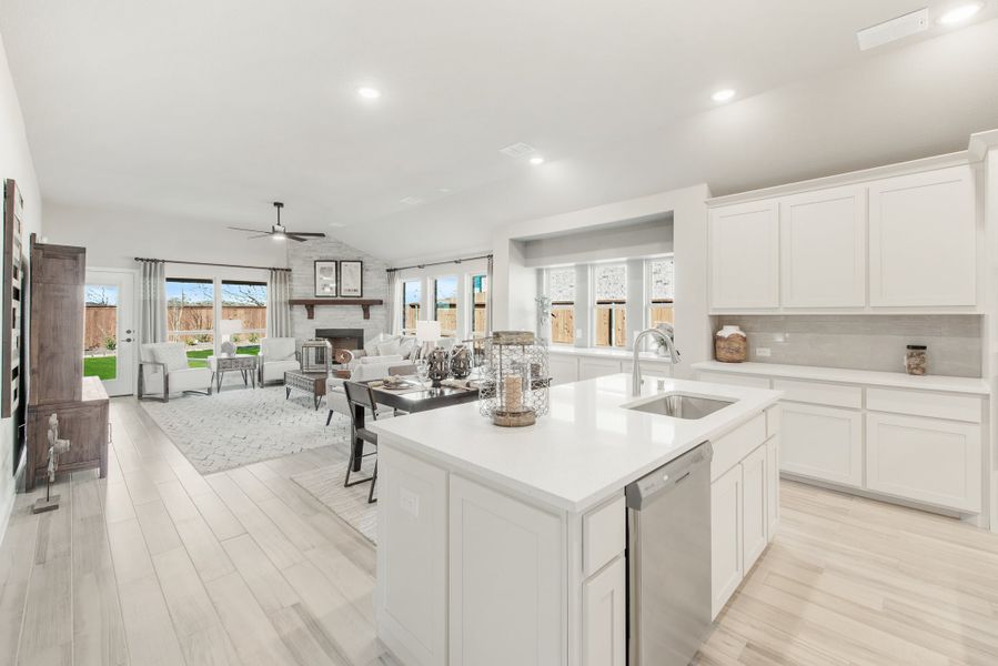 Open-concept kitchen with white cabinets, center island, and living room with fireplace in background