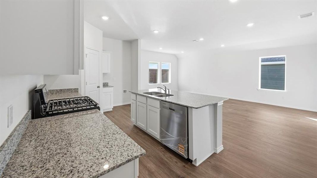Kitchen with light stone countertops, black gas range, a center island with sink, dishwasher, and white cabinets Kitchen with light stone countertops, black gas range, a center island with sink, dishwasher, and white cabinets
