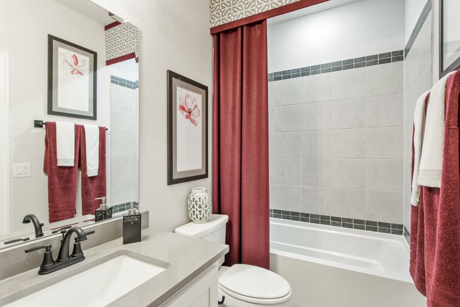 Bathroom with gray countertop vanity, tiled tub-shower combo, and red curtain accents Bathroom with gray countertop vanity, tiled tub-shower combo, and red curtain accents