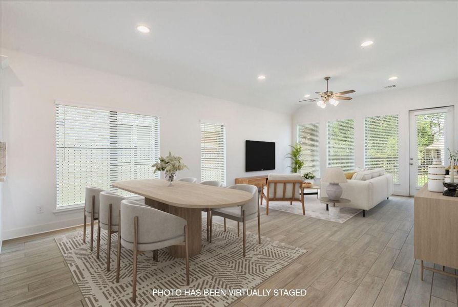 This spacious open-concept living area features light-colored flooring, abundant natural light from numerous windows, and recessed lighting