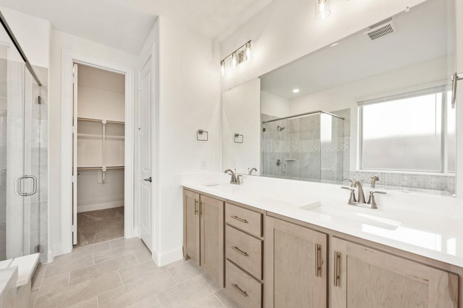 Master bathroom with double vanity, wood cabinets, glass shower, and walk-in closet doorway