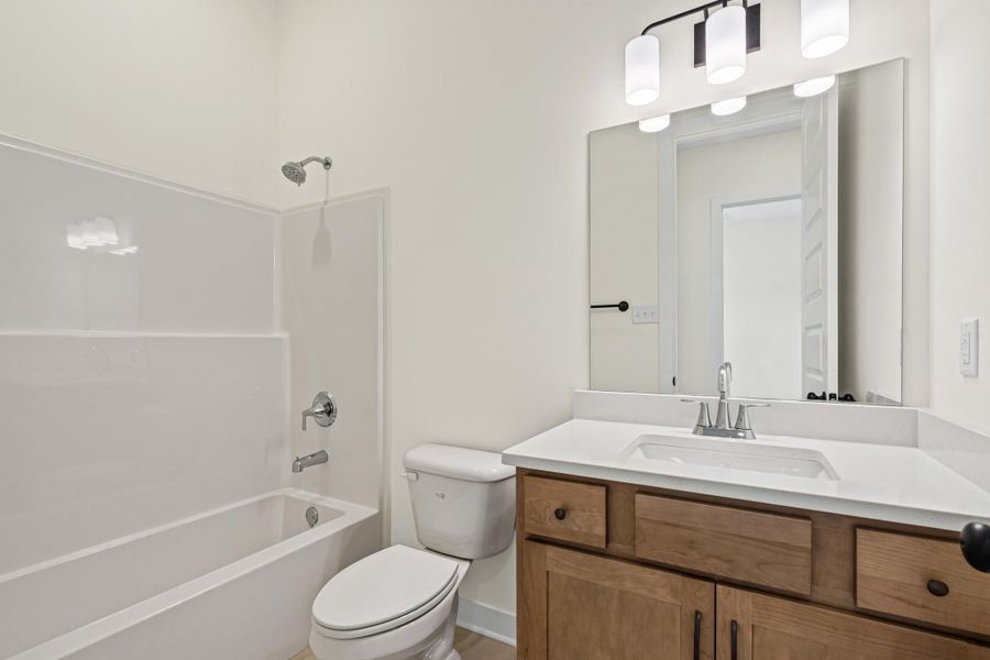 Bathroom featuring a full tub and shower combination, wood-finish vanity with a white countertop, rectangular undermount sink, and a three-light fixture Bathroom featuring a full tub and shower combination, wood-finish vanity with a white countertop, rectangular undermount sink, and a three-light fixture