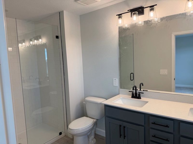 Luxurious primary en suite bathroom with dual vanities and frameless glass shower, featuring the AW Minimalist Collection